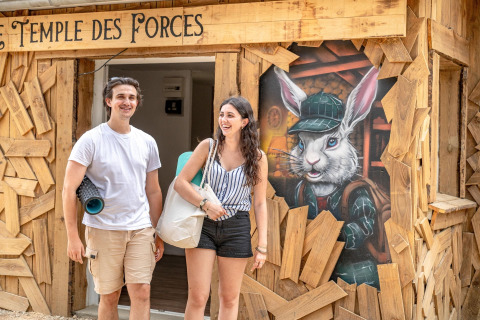 Two smiling people outside the 'TEMPLE DES FORCES' entrance at Flower Camping Au Bois Des Biches, France.