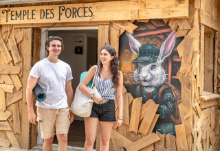 Twee vrolijke mensen aan de ingang van 'TEMPLE DES FORCES' bij Flower Camping Au Bois Des Biches in Frankrijk.