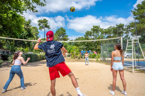 Quattro giovani adulti giocano a beach volley in un villaggio vacanze a Pays de la Loire, Francia, in una giornata soleggiata.