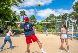 Vier junge Erwachsene spielen Beachvolleyball in einem Ferienpark in Pays de la Loire, Frankreich, bei Sonne.