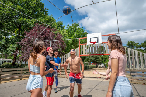 Giovani adulti giocano a basket all'aperto al Flower Camping Au Bois Des Biches, Pays de la Loire, Francia.