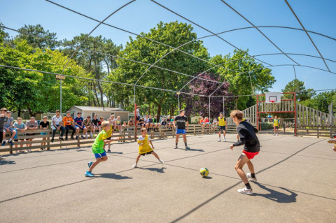 Bambini che giocano a calcio su un campo all'aperto, circondati da spettatori, in un campeggio Pays de la Loire.