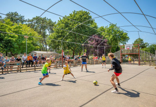 Niños jugando fútbol en una cancha al aire libre, rodeados de espectadores, en un parque vacacional de Pays de la Loire.