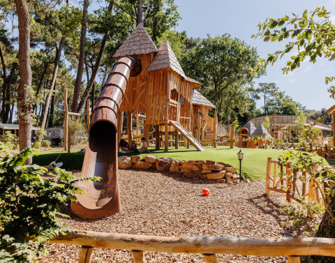 Speelterrein met houten kasteel, glijbaan en gras bij Flower Camping Au Bois Des Biches in Frankrijk.