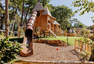 Spielplatz mit Holzburg, Rutsche und Grünfläche im Flower Camping Au Bois Des Biches in Frankreich.