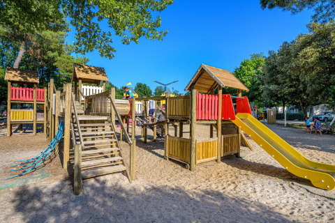 Niños jugando en parque infantil de madera con tobogán en Flower Camping Au Bois Des Biches, Pays de la Loire, Francia.