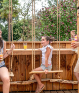 Gezin geniet van drankjes op houten terras met schommels bij Flower Camping Au Bois Des Biches.