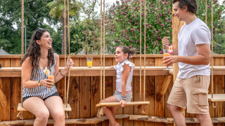 Familie entspannt auf einer Holzterrasse mit Schaukeln und Getränken bei Flower Camping Au Bois Des Biches.