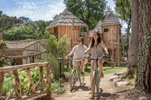 Due persone vanno in bicicletta tra le casette di legno in un villaggio vacanze a Pays de la Loire, Francia.