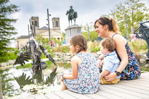 Madre e due bambini seduti vicino a uno stagno a Flower Camping Au Bois Des Biches, Pays de la Loire, Francia.