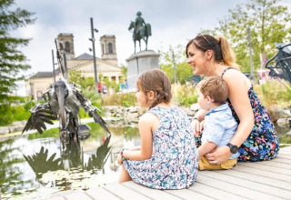 Mother and two children sit by a pond at Flower Camping Au Bois Des Biches, Pays de la Loire, France.