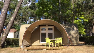 Safari tent Tent Lodge Coco Sweet met houten terras en groene stoelen op een bosrijke kampeerplek.