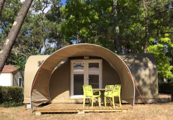 Tenda safari Tent Lodge Coco Sweet con veranda e sedie verdi in un campeggio soleggiato tra gli alberi.