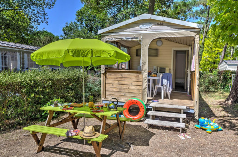 Vista esterna di una tenda safari Cabane Nature con tavolo da picnic, ombrellone verde e giochi colorati.