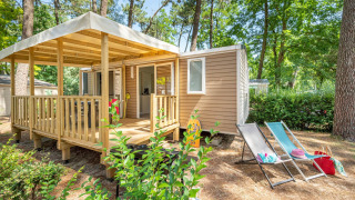 Stacaravan Confort chalet set among trees, featuring a wooden deck, outdoor chairs, and summer decor.