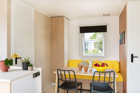 Coin repas moderne et lumineux au chalet Stacaravan Confort avec banquette jaune et jolies plantes.