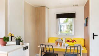 Lichte, moderne eethoek in Stacaravan Confort chalet met gele zithoek en decoratieve planten.