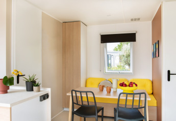 Lichte, moderne eethoek in Stacaravan Confort chalet met gele zithoek en decoratieve planten.