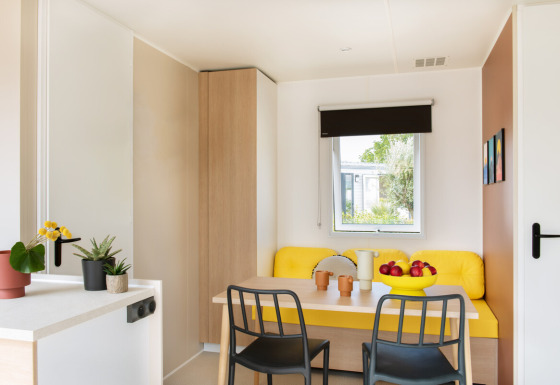 Lichte, moderne eethoek in Stacaravan Confort chalet met gele zithoek en decoratieve planten.