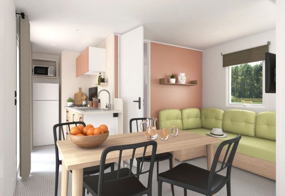 Lichte woonkamer en keuken in het Stacaravan Confort PLUS chalet met eettafel en groene zetel.