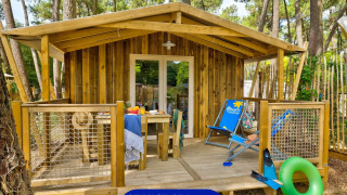 Sweetflower Lodge houten chalet met gezellige veranda, tuinmeubelen en groene bosrijke omgeving.