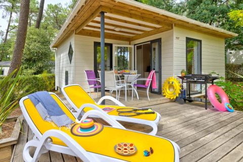 Terrazza assolata di Cottage Premium con lettini gialli, barbecue e tavolo da pranzo all’aperto nel verde.