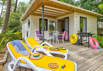 Terraza soleada en Cottage Premium con tumbonas amarillas, barbacoa y comedor exterior rodeado de bosque.