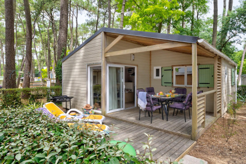 Udendørs udsigt til Cottage Premium hytte med træterrasse, havemøbler og liggestole i skoven.