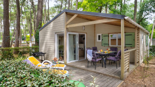 Außenansicht des Cottage Premium mit Holzterrasse, Sitzbereich und Liegestühlen im Wald.