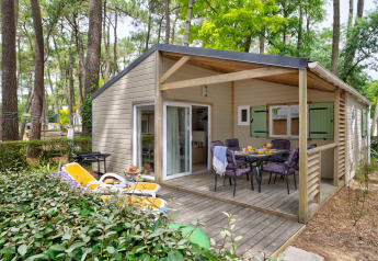 Vista esterna del Cottage Premium con terrazza in legno, tavolo da pranzo e sdraio nel bosco.