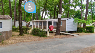 Stacaravan Life Chalet mit barrierefreiem Zugang über eine Rampe, umgeben von Bäumen auf einem Campingplatz.