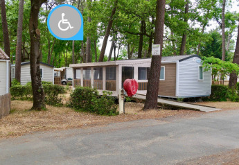 Stacaravan Life Chalet mit barrierefreiem Zugang über eine Rampe, umgeben von Bäumen auf einem Campingplatz.