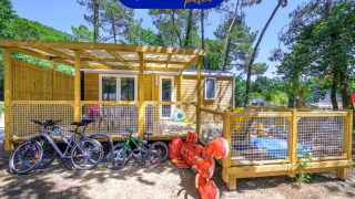 Außenansicht des Stacaravan Family Chalets mit Fahrrädern, Spielplatz und großem Hummer-Spielzeug im Grünen.