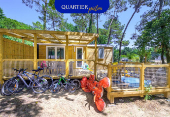 Außenansicht des Stacaravan Family Chalets mit Fahrrädern, Spielplatz und großem Hummer-Spielzeug im Grünen.