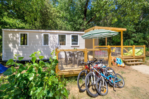 Stacaravan Family chalet with deck, bicycles, and lush green surroundings in a wooded holiday park.