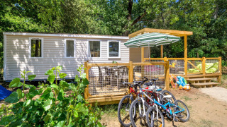 Stacaravan Family Chalet mit Terrasse, Fahrrädern und viel Grün in einem bewaldeten Erholungsgebiet.
