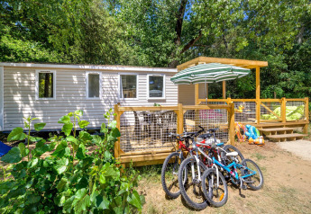 Stacaravan Family Chalet mit Terrasse, Fahrrädern und viel Grün in einem bewaldeten Erholungsgebiet.