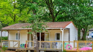 Cottage Family Chalet inmitten grüner Bäume, mit Terrasse und buntem Spielzeug im Garten.