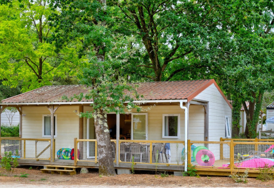 Cottage Family chalet met houten terras, tussen groene bomen en kleurrijk buitenspeelgoed.