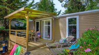 Terrasse der Stacaravan Premium+ Hütte mit Liegestühlen, Esstisch und umgeben von grünen Bäumen.