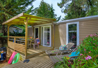 Terrasse der Stacaravan Premium+ Hütte mit Liegestühlen, Esstisch und umgeben von grünen Bäumen.