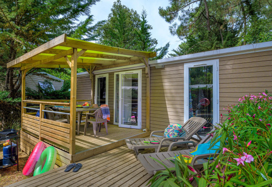 Buitenterras aan Stacaravan Premium+ chalet met ligstoelen, eettafel en omgeven door groene bomen.