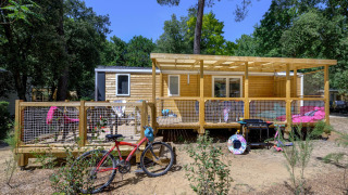 Vue extérieure du chalet Stacaravan Family avec terrasse en bois, vélo et mobilier extérieur, entouré d’arbres.