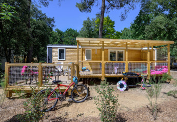 Außenansicht von Stacaravan Family Chalet mit Holzterrasse, Fahrrad und Gartenmöbeln im Grünen.
