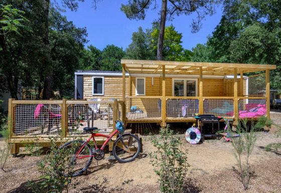 Außenansicht von Stacaravan Family Chalet mit Holzterrasse, Fahrrad und Gartenmöbeln im Grünen.