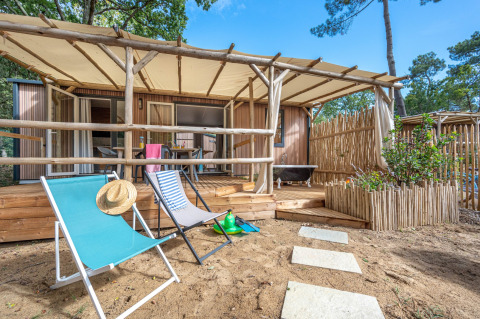 Stacaravan Garden chalet met houten terras, strandstoelen en zandomgeving, omringd door natuur.