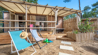 Stacaravan Garden chalet met houten terras, strandstoelen en zandomgeving, omringd door natuur.