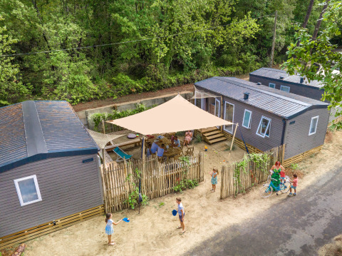 Luchtfoto van glamping accommodatie met moderne chalets, gezinnen genieten buiten onder een zonnescherm.