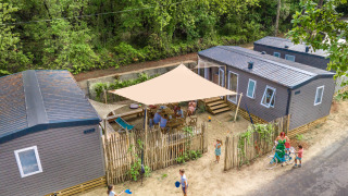 Luftaufnahme von Glamping-Unterkünften, moderne Hütten, Familie genießt Zeit im Freien unter Sonnensegel.
