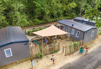 Vista aerea di un alloggio glamping con cabine moderne, famiglie che si godono attività all'aperto sotto un telo.